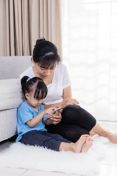 Aziatische Chinese moeder en dochter met behulp van smartphone op de grond — Stockfoto