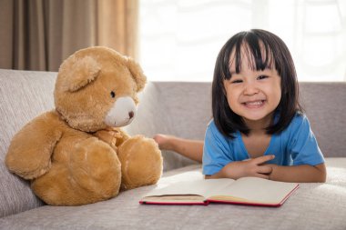 Oyuncak ayı ile Asya Çinli küçük kız okuma kitabı gülümseyen