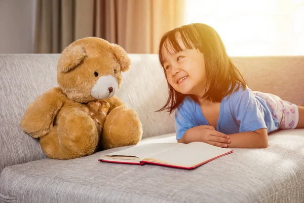 Glimlachend Aziatische Chinese kleine meisje leesboek met teddybeer — Stockfoto