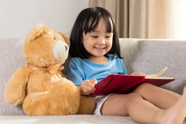 Uśmiechający się azjatycki chiński mały dziewczyna czytania książki z misiem — Zdjęcie stockowe