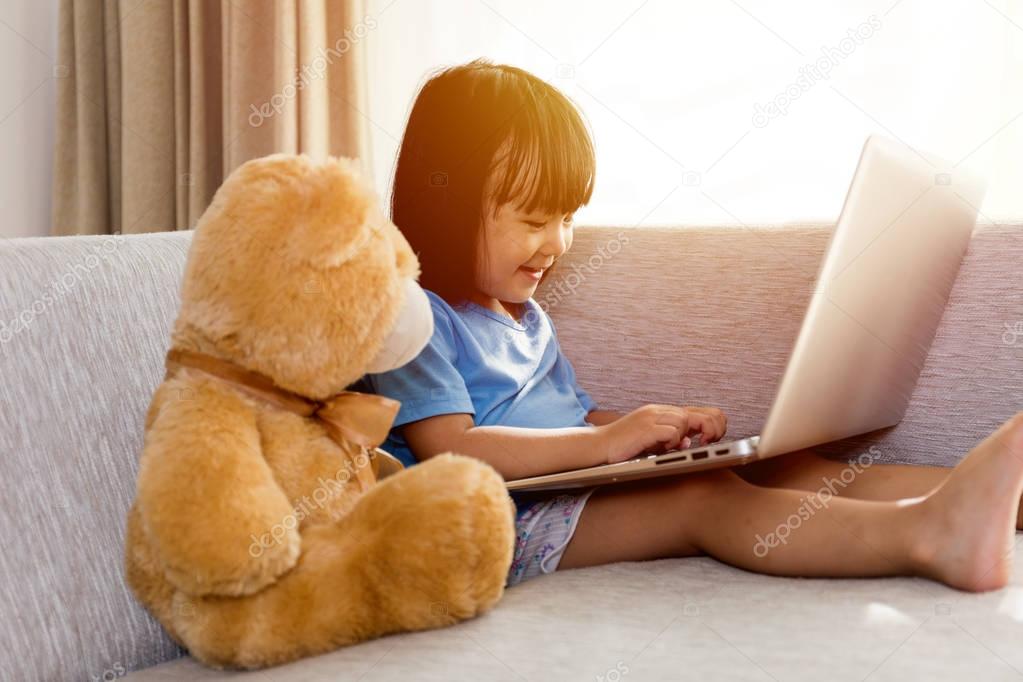 Asian Chinese little girl using laptop with teddy bear