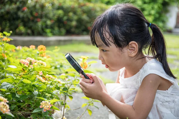 拡大鏡を通して花を見て中国のアジアの少女 — ストック写真