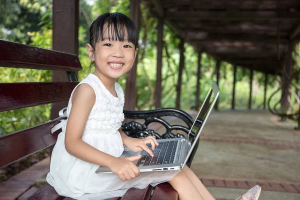 Asijská Čínská holčička sedí na lavičce s notebookem — Stock fotografie
