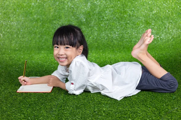 Asiatische chinesische kleines Mädchen liegt auf dem Gras und schreibt — Stockfoto