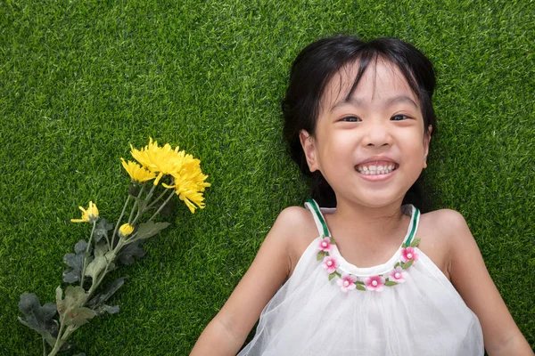 Asijská Čínská holčička ležící na trávě s květinami — Stock fotografie