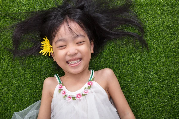 Asiática chinesa menina deitada na grama com flor — Fotografia de Stock