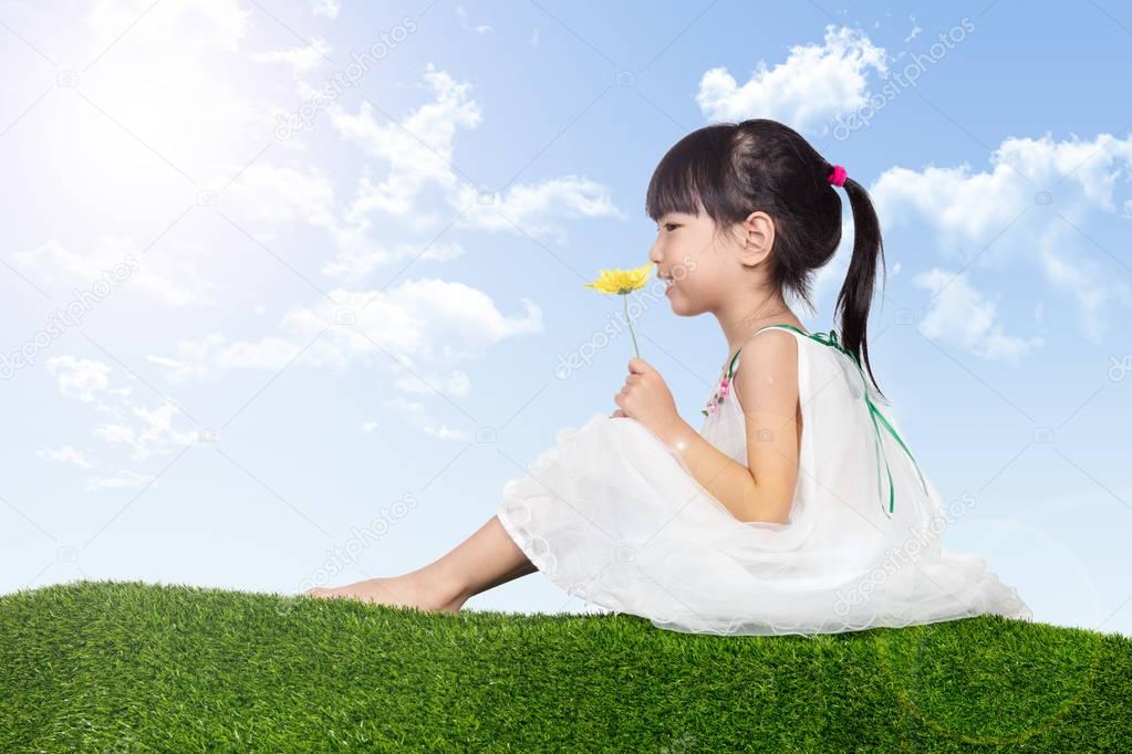 Asian Chinese girl sitting on the grass and holding flowers