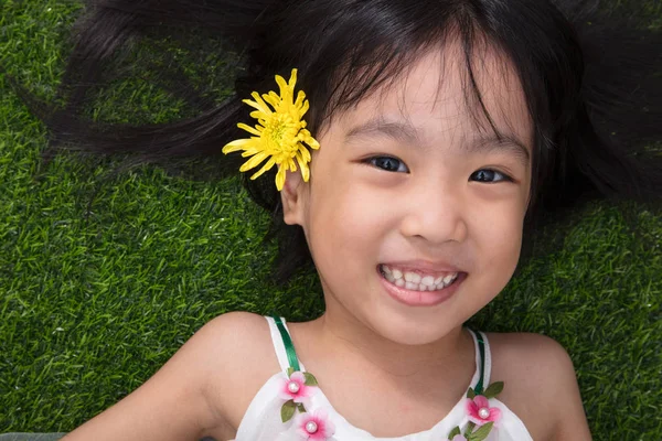 Asijská Čínská holčička ležící na trávě s květinou — Stock fotografie