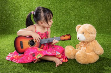 Asyalı küçük Çinli kız oyuncak ayı ile gitar çalmak