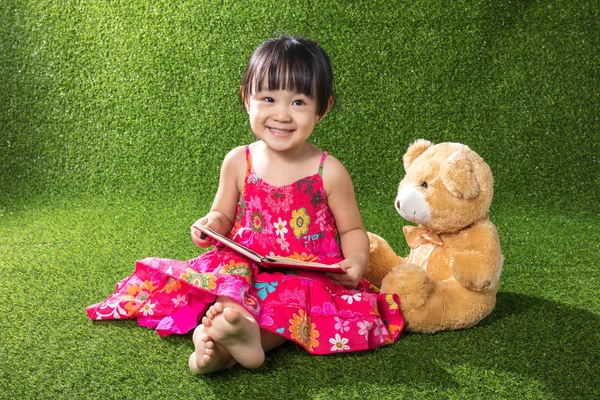 Asiático chinês menina leitura livro com ursinho de pelúcia — Fotografia de Stock