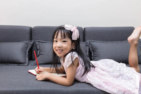 Azjatycki chiński dziewczynka leżąc na kanapie pisania książki — Zdjęcie stockowe