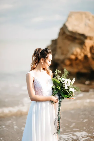 Sposa con un bouquet da sposa sulla riva del mare — Foto Stock