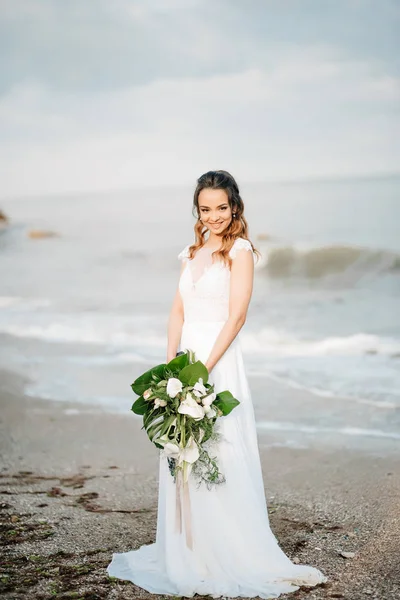 Sposa con un bouquet da sposa sulla riva del mare — Foto Stock