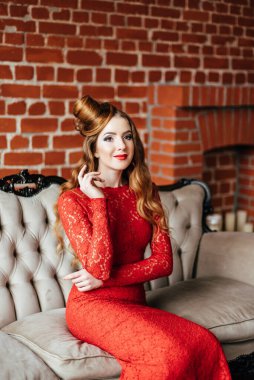 Antik bir kanepede parlak bir odada parlak kırmızı elbiseli kızıl saçlı genç bir kız.