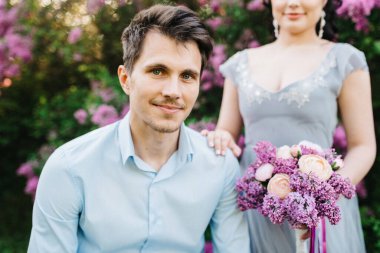 Bir adam ve bir kız düğün töreninden önce leylakların bahar bahçesinde yürüyorlar.