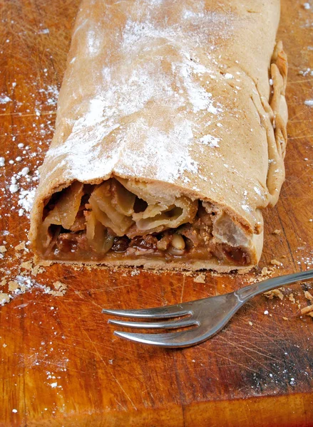 Strudel aux pommes fait maison et une fourchette sur une planche à découper en bois . — Photo