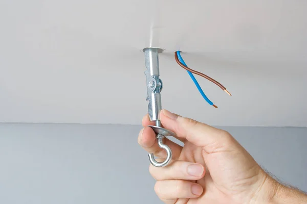 Handyman mounting a light fixture for a ceiling lamp using a toggle bolt.