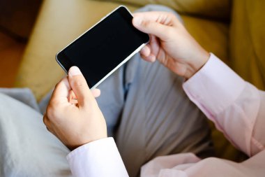 Closeup üstünde hareket eden telefon kanepede oturan adamın elinde. Üst yan görünümü arka plan sahte