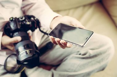 Cep telefonu ve holding Dslr kamera el üzerinde kapalı arka plan kullanan adam.