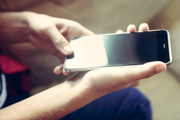 Closeup on mobile phone in hand of young woman sitting on couch. Top side view mock up background