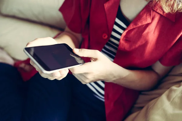 Closeup on mobile phone in hand of young woman sitting on couch. Top side view mock up background