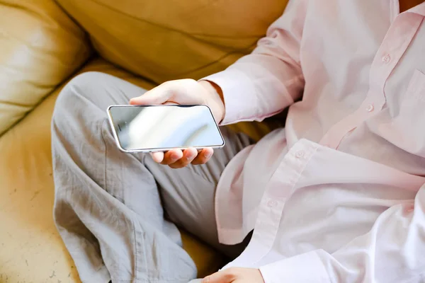 Closeup on mobile phone in hand of man sitting on couch. Top side view mock up background