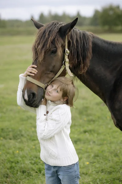 Młoda dziewczynka w biały sweter i dżinsy przytulił głowę konia w gospodarstwie ciepły jesienny dzień. Portret styl życia — Zdjęcie stockowe