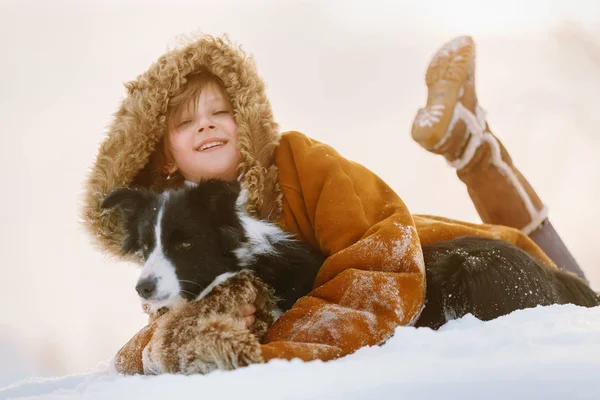 Hermosa niña abrazando a un perro en invierno en la nieve Frontera collie y sonriendo — Foto de Stock