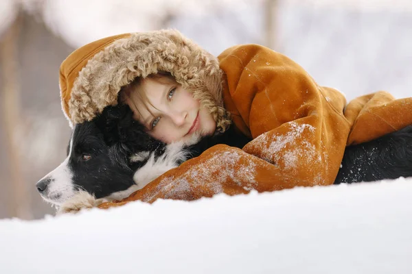 Kis fiatal lány fekete-fehér kutya átölelve a hóban, és mosolyogva Stock Fotó