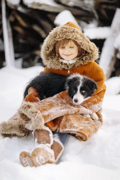 Joven niña sentada en un abrigo de piel de invierno en la nieve y se mantiene en el perro faldero al aire libre — Foto de Stock