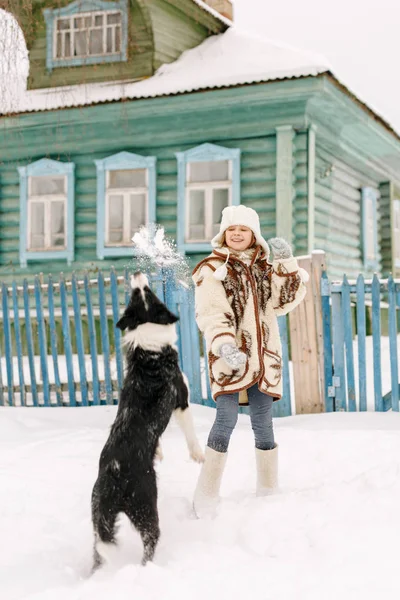 Sonriente linda niña jugando en la nieve en frente de la casa en invierno con negro y blanco frontera collie perro crianza — Foto de Stock