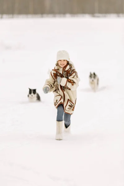 Niña corriendo en la nieve en botas y abrigo, y sus dos perros borde collie — Foto de Stock