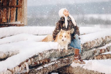 Bir kürk manto ve şapka açtığında kış sevgili köpeği yanında oturan sevimli güzel kız çocuk onun etrafında hugs ve yumuşak kar gider