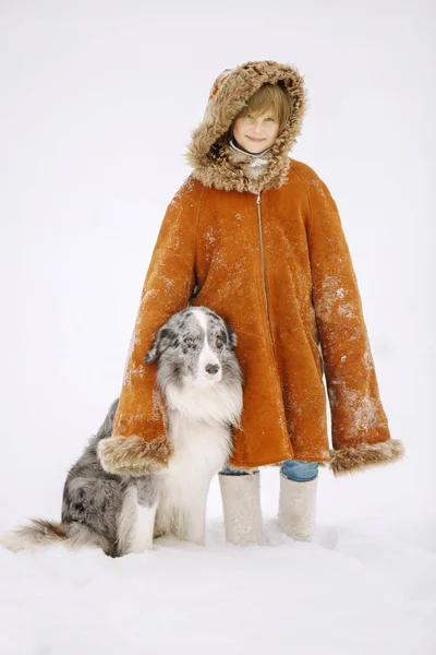 Niña pequeña en el abrigo de piel roja de su madre en el invierno la nieve de pie junto a un perro Border Collie y sonriendo — Foto de Stock