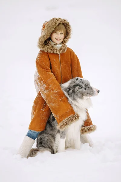 Joven niña sonriente bebé en invierno en la nieve en puestos de abrigo de piel roja y abrazo perro mascota Frontera Collie — Foto de Stock