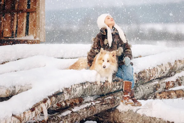 Aranyos szép lány gyermek egy bunda és sapka ült a naplók szeretett kutyája mellett télen ölelést őt körül, és megy a puha hó Jogdíjmentes Stock Fotók