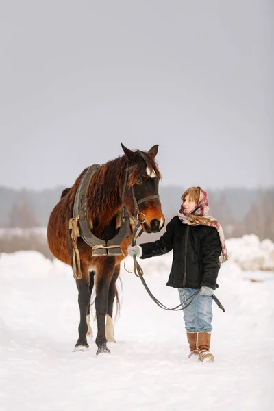 Ragazzina in inverno sulla neve in pelliccia e velo conduce il cavallo per la briglia e guardandolo — Foto Stock