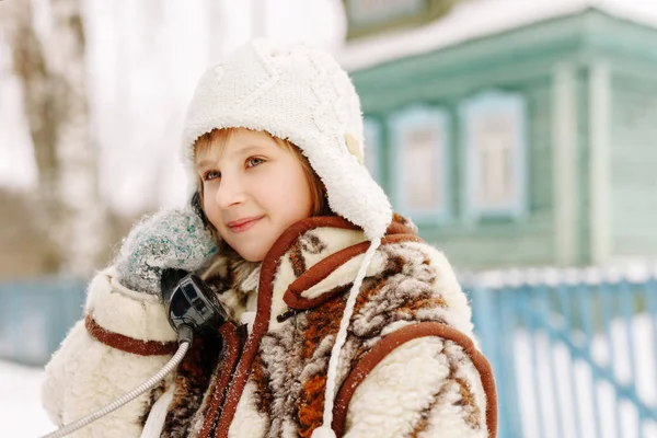 Joven chica encantadora en un abrigo de piel, sombrero y manoplas en las llamadas de invierno hablando por el teléfono viejo y sonriendo — Foto de Stock
