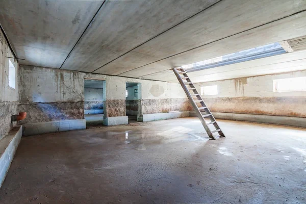 Tamamlanmamış garaj bodrum katının beton döşemesi merdiven ve dikim günü pencere ışığıyla çöp renginde.