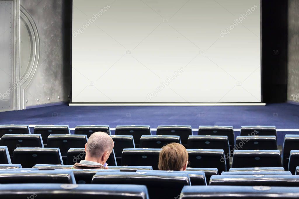 Few people in an empty blue cinema hall waiting unpopular movie