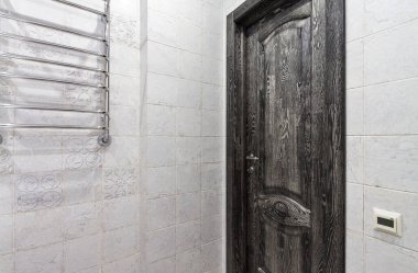 Banyonun beyaz kaplamalı mozaik duvarında klasik kapalı siyah meşe kapısı.