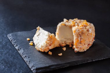 Koyu siyah arka planda taze crotten çiftlik keçi peyniri ve mango, fındık ve ananas parçaları.