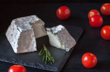 Damarlı yumuşak Fransız keçi peyniri dilimlenmiş ve kırmızı kiraz domatesli biberiye dalı siyah arka planlı.