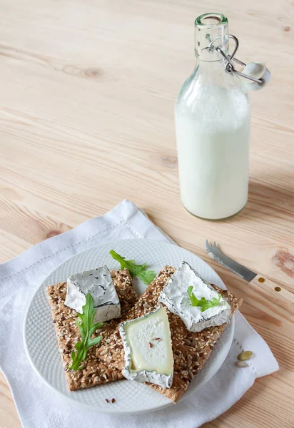 Plate crispbread with soft slices ash goat cottage cheese with arugula and full bottle goat milk wooden background copy space