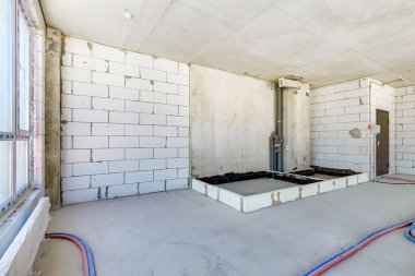 Konut binasının inşaat şantiyesiymiş. Yeni evin içinde panoramik pencere ve yerde elektrik kabloları olan beyaz tuğla duvar var..