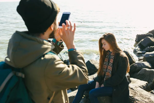 Schöne und stilvolle Paar werden an einem felsigen Strand fotografiert. Paar in Jacken, Hüten und Stiefeln — Stockfoto