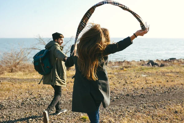 Beautiful and stylish couple walking on a rocky beach. Couple dressed in jackets, hats and boots — Stock Photo, Image