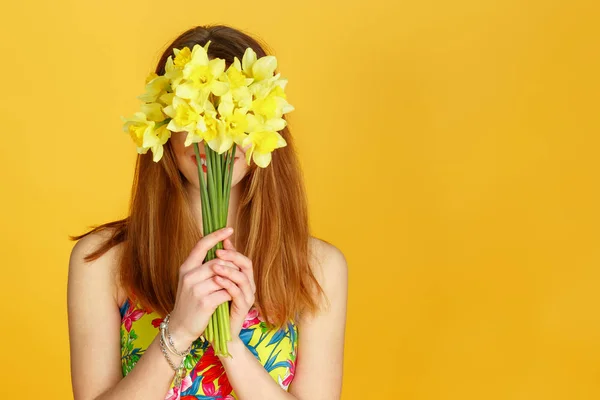 Kvinnan håller gula blommor och gömmer sig bakom det mot gul vägg — Stockfoto