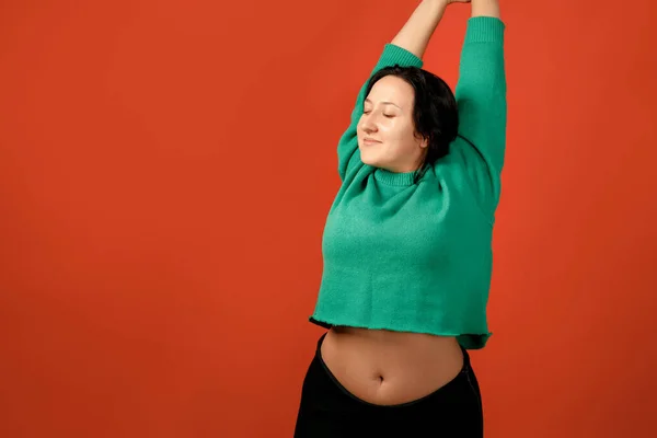 Happy plus size positive woman. Happy body positive concept. I love my body. Attractive overweight woman posing on camera in the studio on a colored background. Girl wearing a sweater
