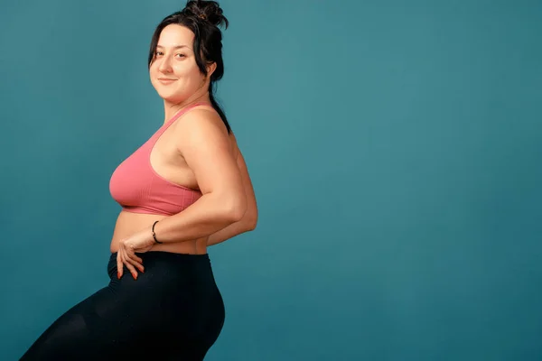 Happy plus size positive woman. Happy body positive concept. I love my body. Attractive overweight woman posing on camera in the studio on a colored background. Girl is wearing a coral bra